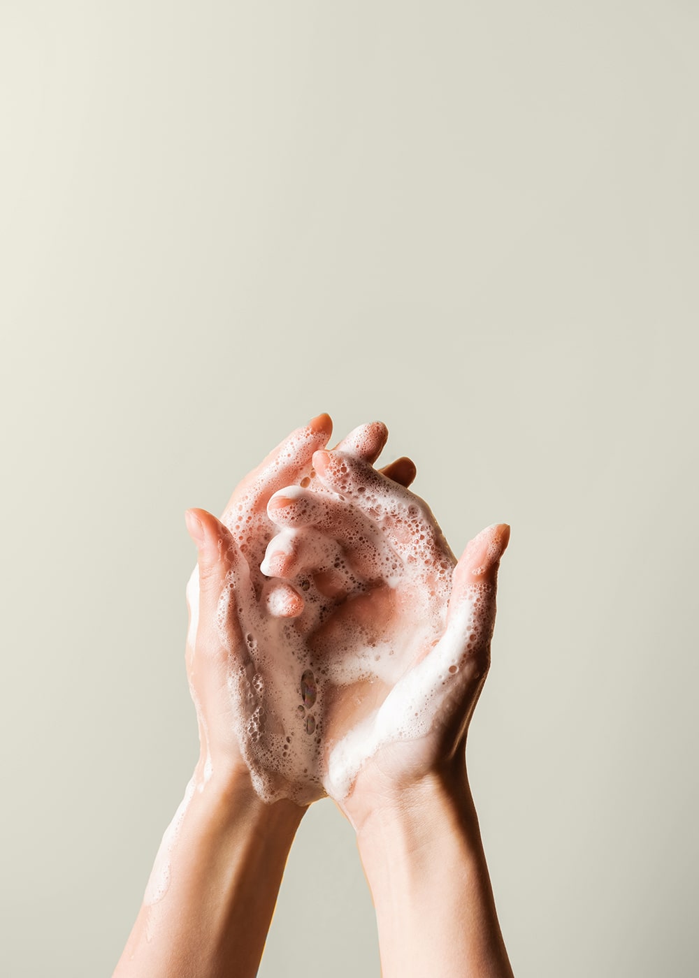 Hände mit Schaum vom Händewaschen und Handseife vor beigener Wand