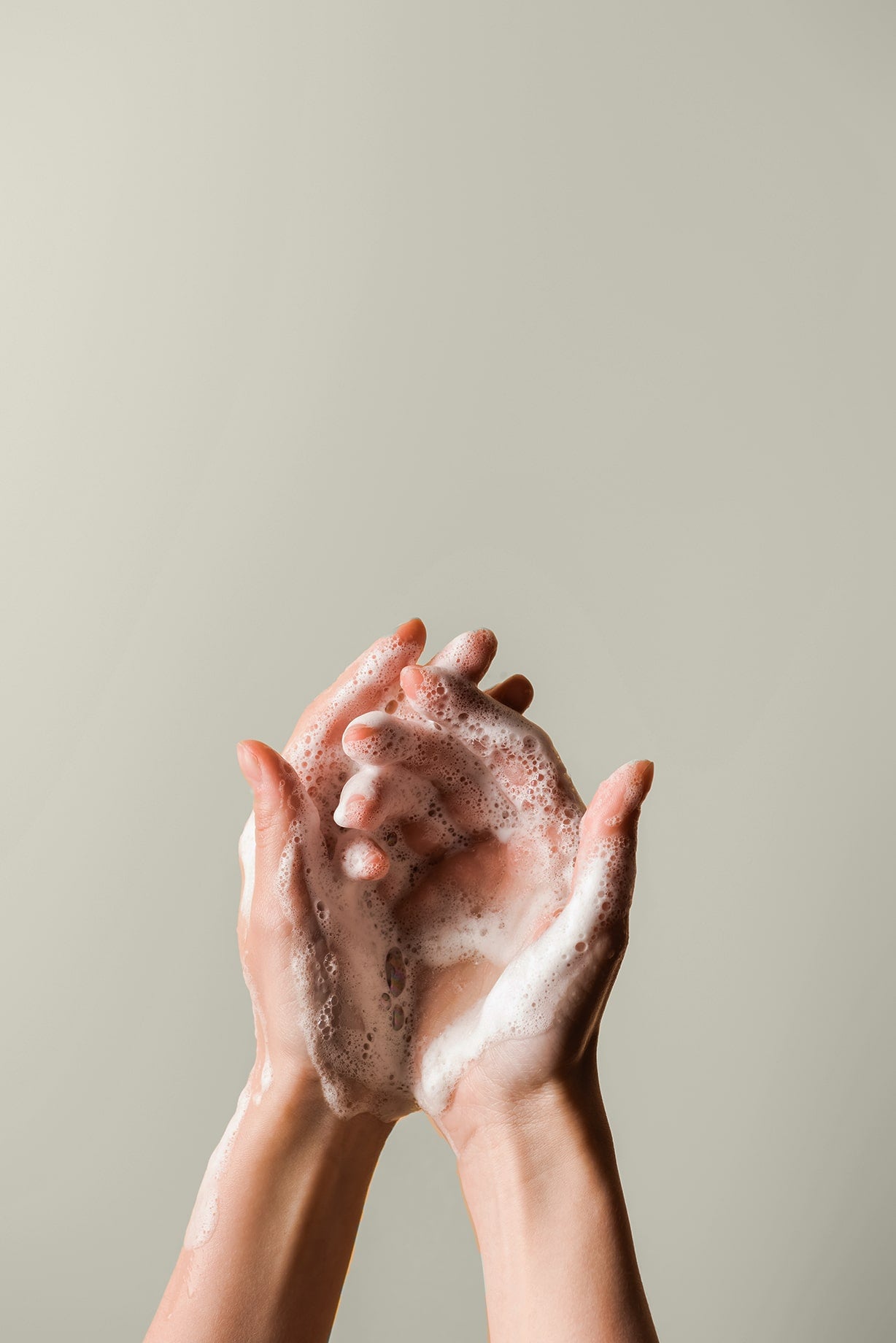 Hände mit Schaum vom Händewaschen vor beigener Wand