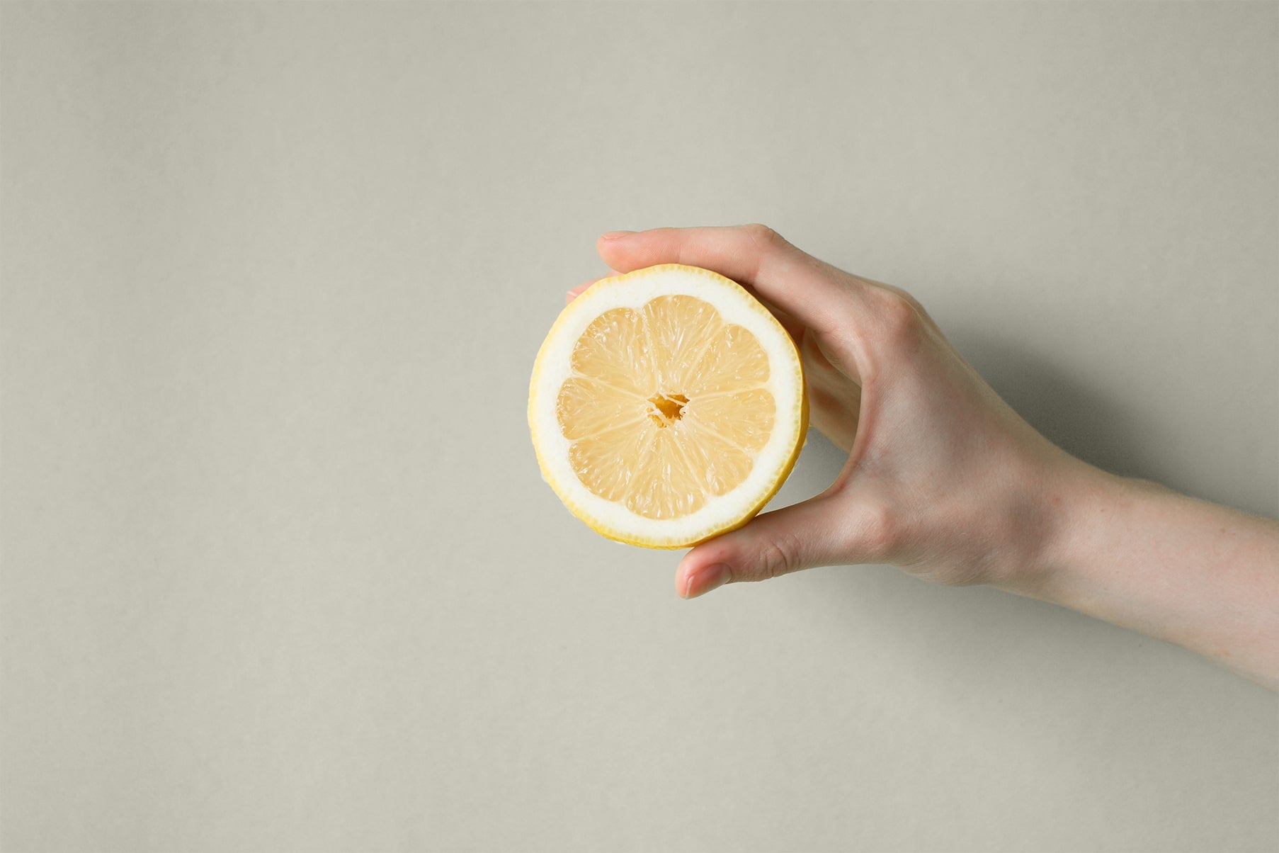 Zitrone in der Hand vor einer beigenen Wand